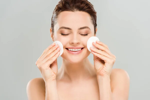 Cheerful naked woman with closed eyes holding cotton pads isolated on grey — Stock Photo