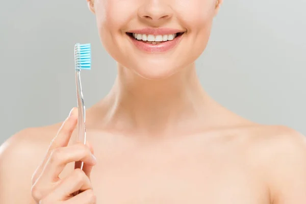 Обрізаний вид гола жінка посміхається і тримає зубну щітку ізольовано на сірому — стокове фото
