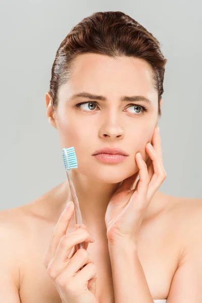 Femme bouleversée touchant le visage et tenant la brosse à dents isolée sur gris — Photo de stock