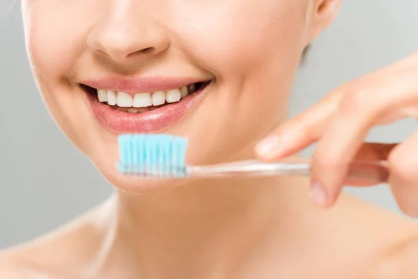 Enfoque selectivo de la mujer sonriendo y sosteniendo cepillo de dientes aislado en gris - foto de stock