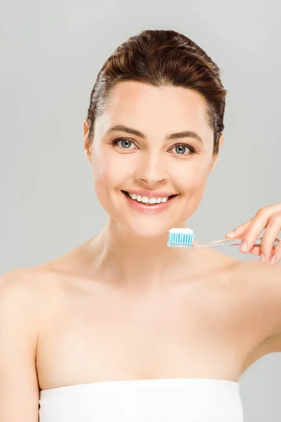 Mujer alegre sonriendo mientras sostiene el cepillo de dientes con pasta de dientes aislada en gris - foto de stock