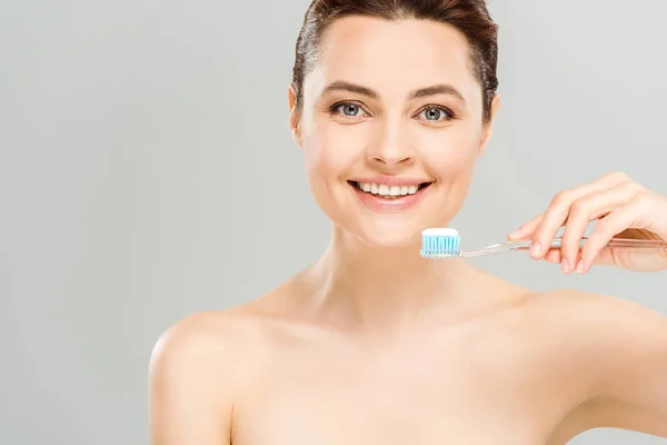 Весела гола жінка посміхається, тримаючи зубну щітку з зубною пастою ізольовано на сірому — стокове фото