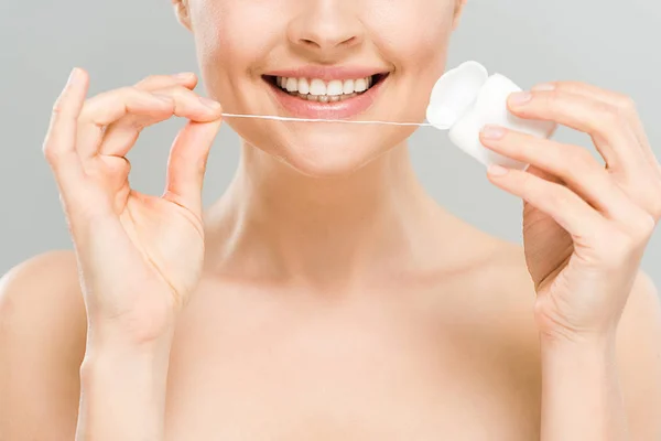 Vue recadrée d'une femme nue gaie tenant du fil dentaire près de dents isolées sur gris — Photo de stock