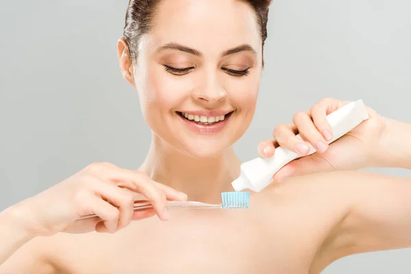 Весела гола жінка тримає зубну пасту біля зубної щітки ізольована на сірому — стокове фото