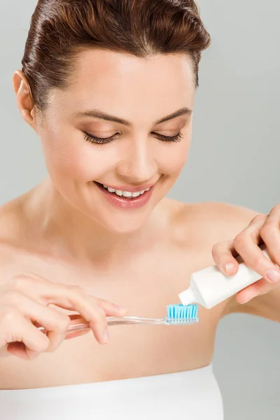 Cheerful woman holding toothpaste near toothbrush isolated on grey — Stock Photo