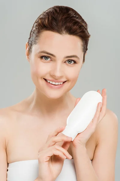 Happy woman holding bottle of body lotion isolated on grey — Stock Photo