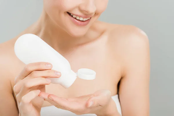 Cropped view of cheerful woman applying body lotion while holding bottle isolated on grey — Stock Photo