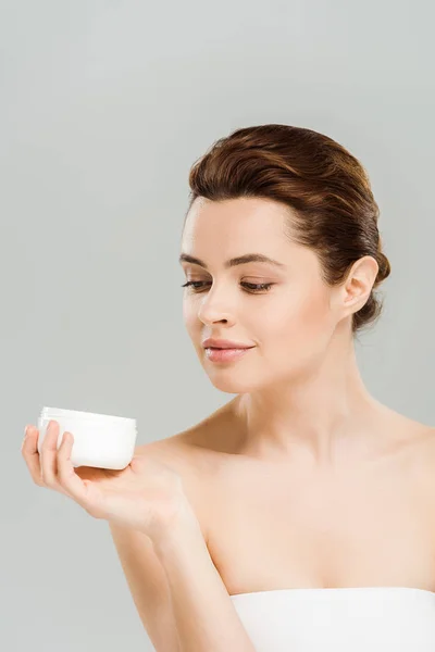 Hermosa mujer sosteniendo contenedor con crema cosmética aislado en gris - foto de stock