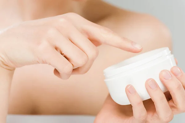 Vista ritagliata della donna che punta con il dito al contenitore con crema per il viso isolata su grigio — Foto stock