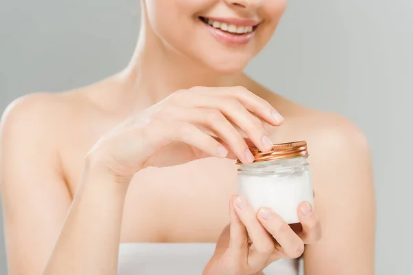 Vista recortada de la mujer feliz sosteniendo contenedor con crema cosmética aislado en gris - foto de stock