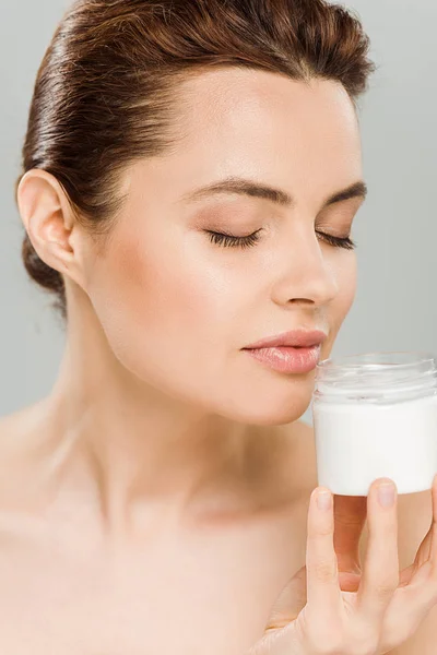 Attractive woman smelling face cream and holding container isolated on grey — Stock Photo