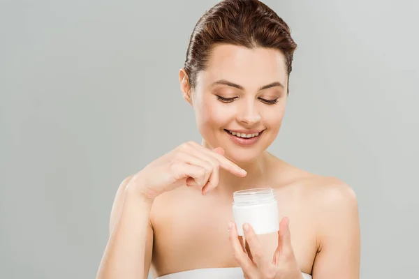 Happy woman pointing with finger at container with face cream isolated on grey — Stock Photo