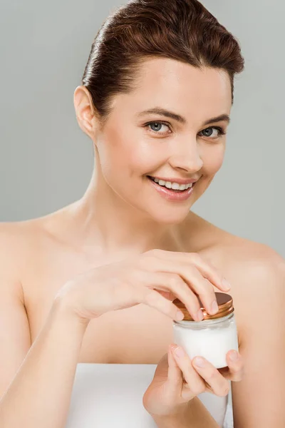 Mulher sorrindo segurando recipiente com creme facial isolado em cinza — Fotografia de Stock