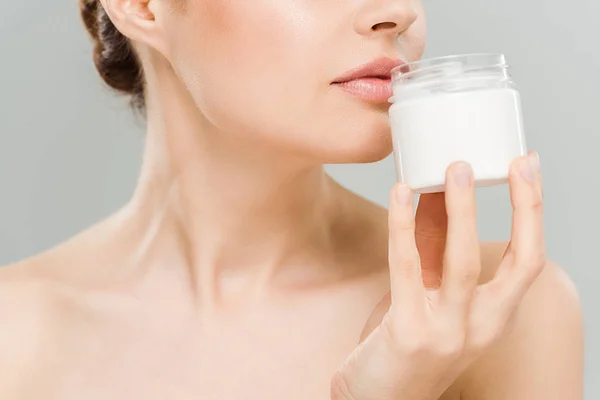 Vista ritagliata di donna nuda che tiene contenitore con crema per il viso vicino al viso isolato su grigio — Foto stock