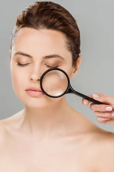 Naked woman with closed eyes holding magnifying glass near face isolated on grey — Stock Photo