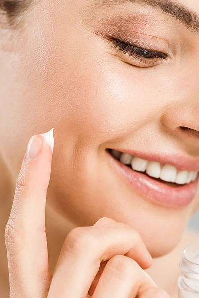 Close up of cheerful woman smiling while applying face cream — Stock Photo
