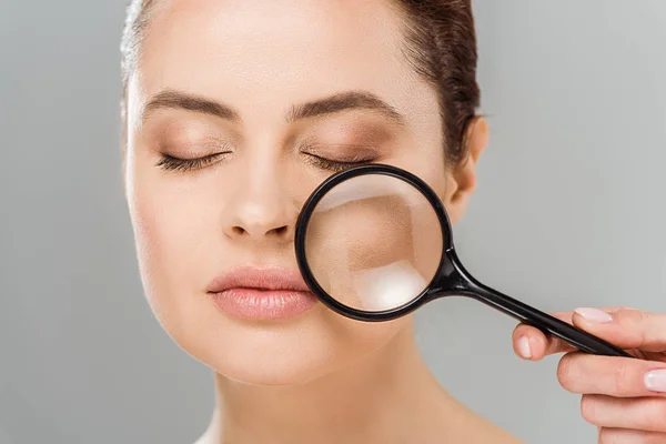 Attraente donna con gli occhi chiusi tenendo lente d'ingrandimento vicino al viso isolato su grigio — Foto stock