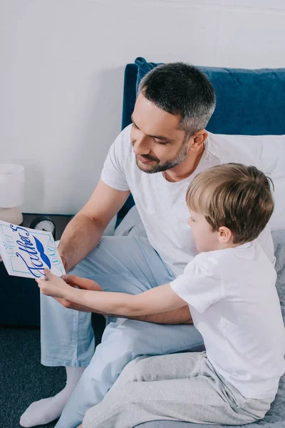 Niño regalando tarjetas de felicitación del día de padres hechos a mano a padre feliz - foto de stock