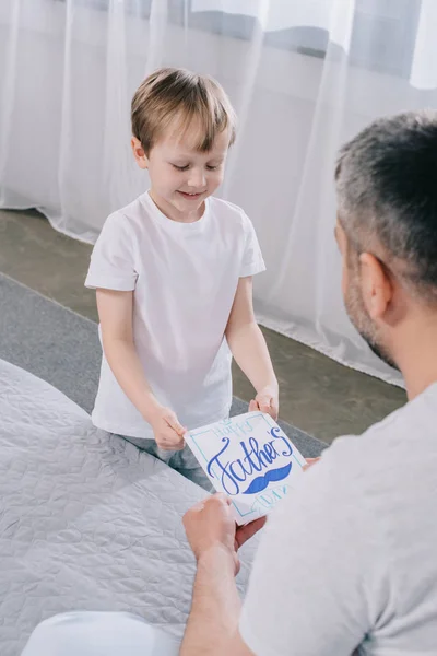 Entzückender Junge lächelt und beschenkt Papas Glückwunschkarte zum Vatertag — Stockfoto