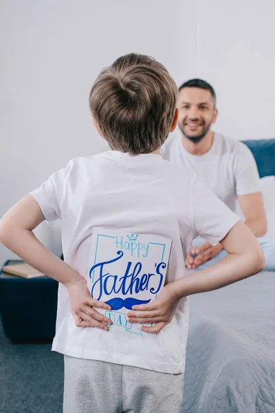 Selektiver Fokus des Sohnes, der eine Grußkarte zum Vatertag in der Hand hält, während er neben dem lächelnden Papa steht — Stockfoto