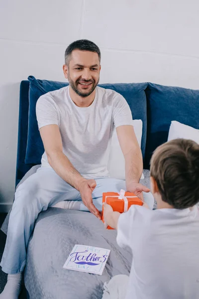 Atrás vista de niño presentando padre día regalo caja a papá feliz - foto de stock