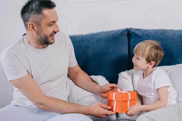 Cute boy presenting gift box for fathers day to smiling daddy — Stock Photo