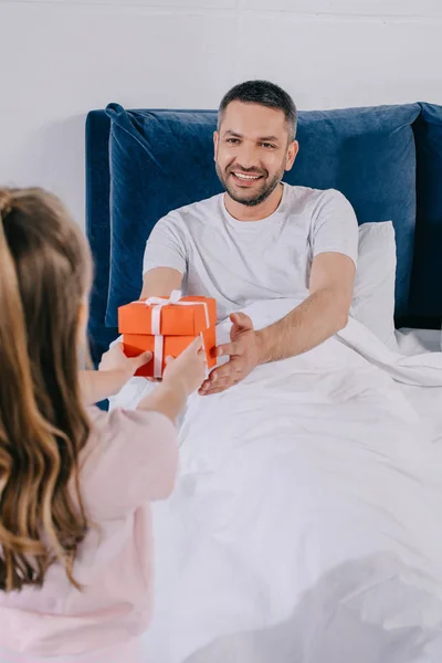 Daughter presenting father day gift box to happy dad sitting under blanket — Stock Photo