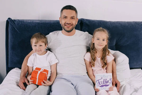 Glücklicher Mann umarmt entzückenden Sohn und Tochter mit Geschenk-Box und Vatertag Grußkarte — Stockfoto