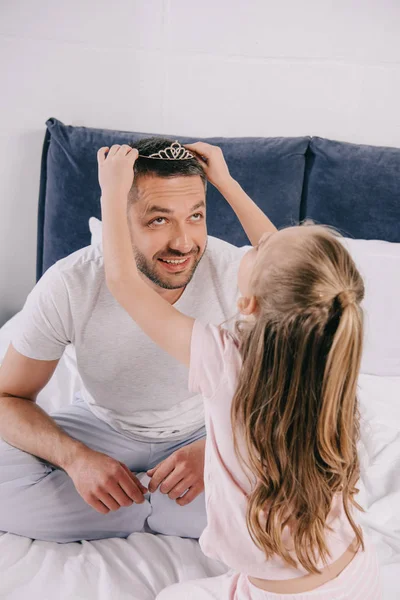 Cute daughter putting diadem on smiling daddy on fathers day — Stock Photo