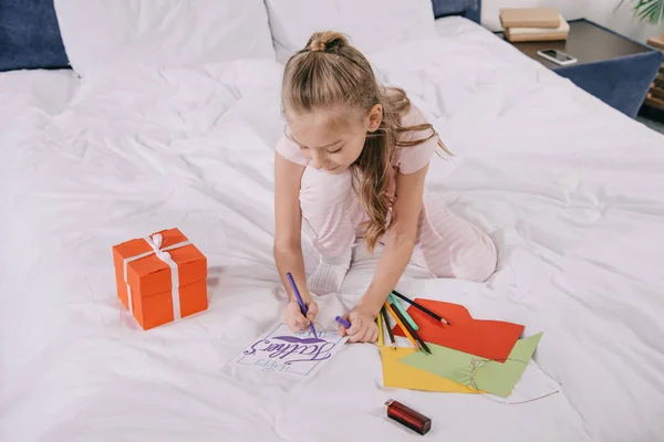 Entzückendes Kind zeichnet am Vatertag Grußkarte in der Nähe von Geschenkbox und bunten Blättern Papier — Stockfoto