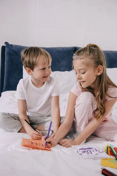 Adorable children drawing fathers day greeting cars while sitting on bedding — Stock Photo