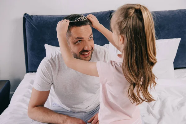 Cute daughter putting diadem on happy dad on fathers day — Stock Photo