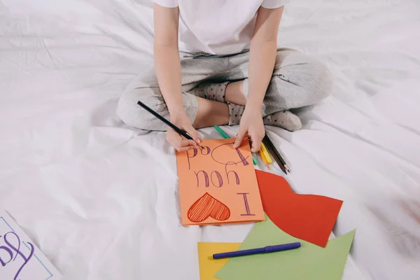 Partial view of kid drawing fathers day greeting card while sitting on bed — Stock Photo