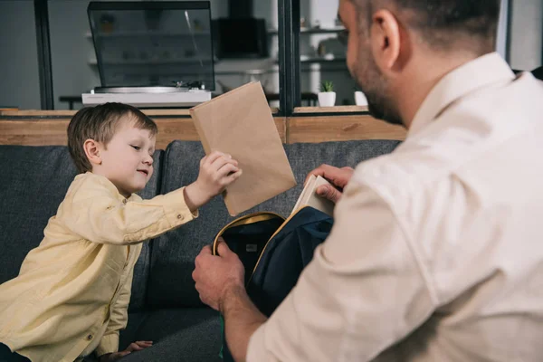 Aufmerksamer Vater hilft Sohn beim Einpacken von Buch in Rucksack zu Hause — Stockfoto