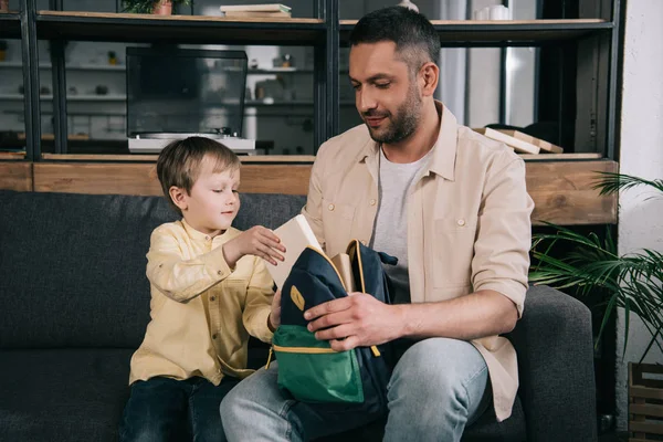 Feliz padre ayudando adorable hijo embalaje libro en mochila - foto de stock