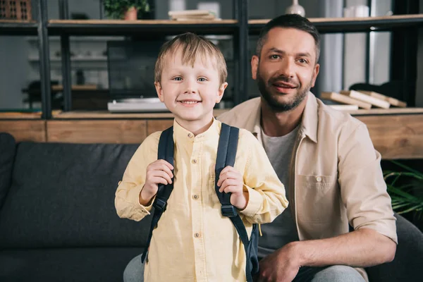 Smiling boy with backpack on shoulders smiling at camera together with happy dad — Stock Photo
