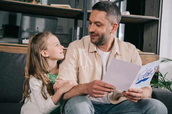 Entzückende Tochter umarmt Vater mit Vatertags-Grußkarte — Stockfoto