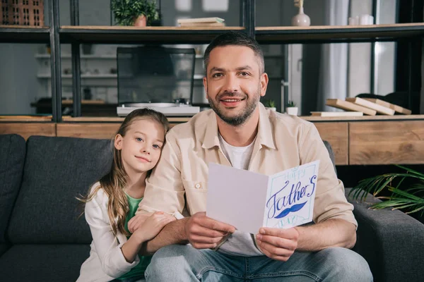 Niedliche Tochter lächelnder Vater hält Grußkarte zum Vatertag und lächelt in die Kamera — Stockfoto