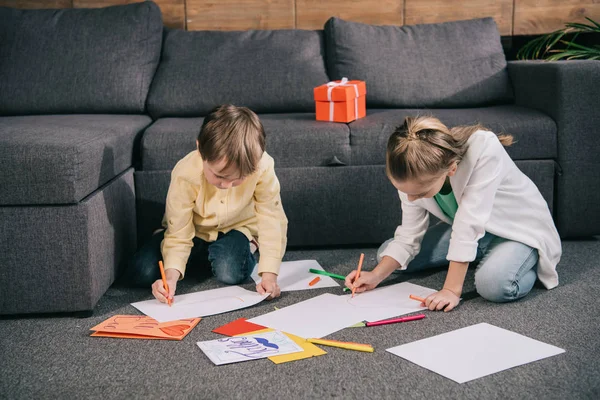 Brother and sister sitting on floor and drawing on white paper sheets — Stock Photo