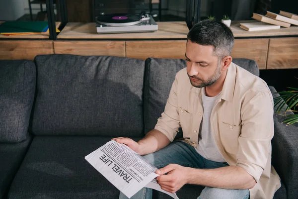 Aufmerksamer Mann liest Zeitung im Reiseleben, während er zu Hause auf dem Sofa sitzt — Stockfoto