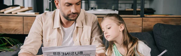 Panoramic shot of father and adorable daughter reading business newspaper together — Stock Photo