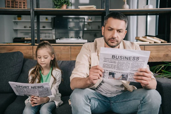 Concentrated father and daughter reading sport news and business newspapers at home — Stock Photo