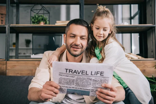 Adorable child hugging father reading travel life newspaper at home — Stock Photo