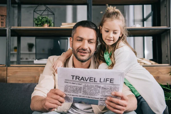 Adorable niño abrazo padre leyendo viaje vida periódico en casa - foto de stock