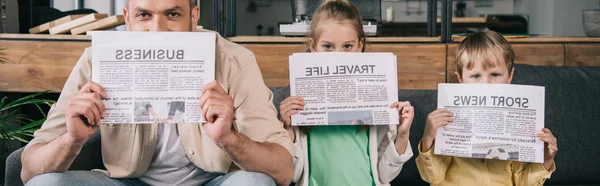 Panoramic shot of cheerful father and kids covering faces with newspapers — Stock Photo