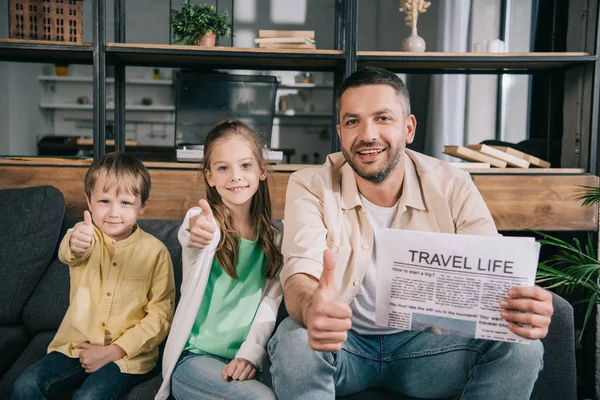 Família feliz mostrando polegares para cima, enquanto o pai segurando viagem vida jornal — Fotografia de Stock