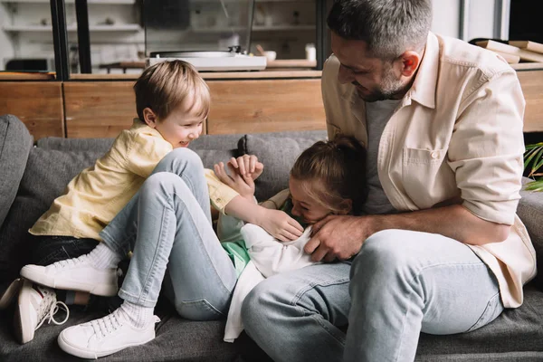 Щасливий батько з веселими дітьми розважається на день батька на дивані вдома — стокове фото