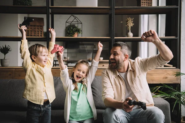 KYIV, UKRAINE - MAY 10, 2019: Happy family celebrating triumph while playing video game with joysticks at home. — Stock Photo