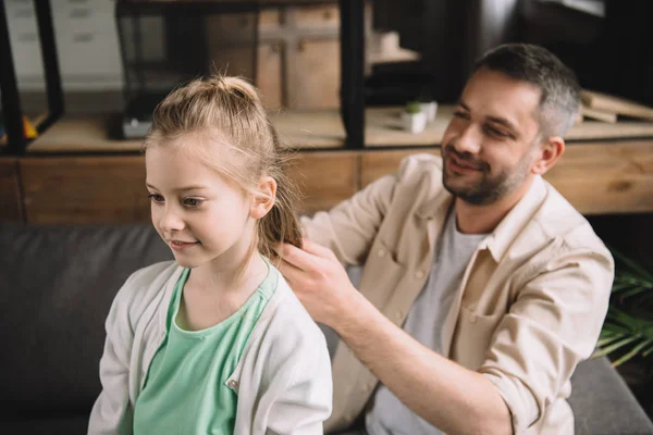 Selective focus of happy father weaving daughters hair at home — Stock Photo