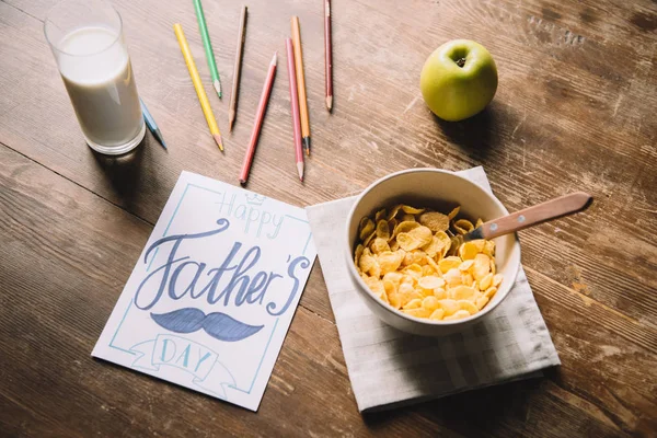 Открытки на день отца, разноцветные карандаши, миска с хлопьями, свежее яблоко и стакан молока на деревянном столе — стоковое фото